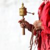 Mönch hält Gebetsmühle und Mala in der Hand